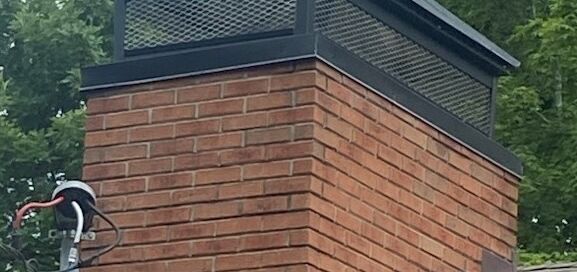 House roof with chimney cap installed on brick chimney roof.